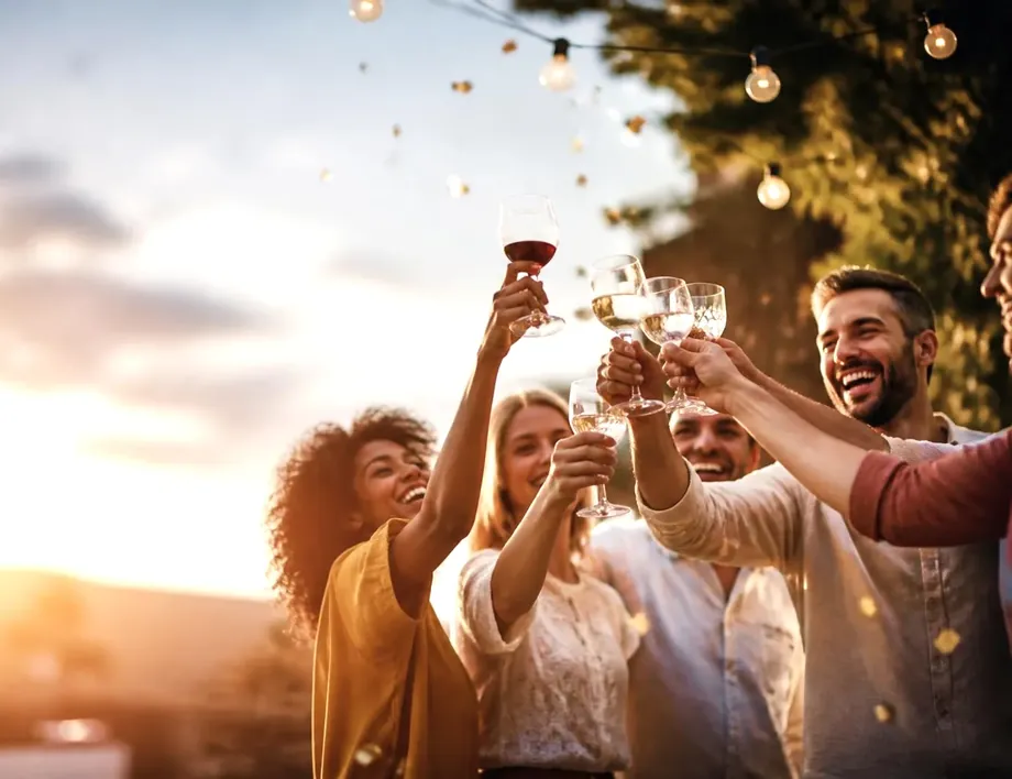 Friends raising glasses together at sunset under string lights